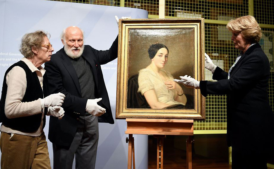 Os herdeiros Maria de las Mercedes Estrada (E) e Wolfgang Kleinertz (C) entregam ao Comiss&aacute;rio do Governo Federal da Fran&ccedil;a Monika Gruetters (D) a pintura saqueada pelos nazistas  intitulada "retrato de um mulher sentada"pelo artista Thomas Couture em B